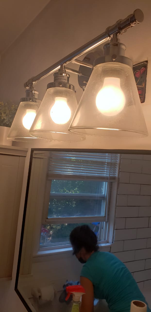 Three-bulb bathroom light fixture with dusty glass shades before cleaning