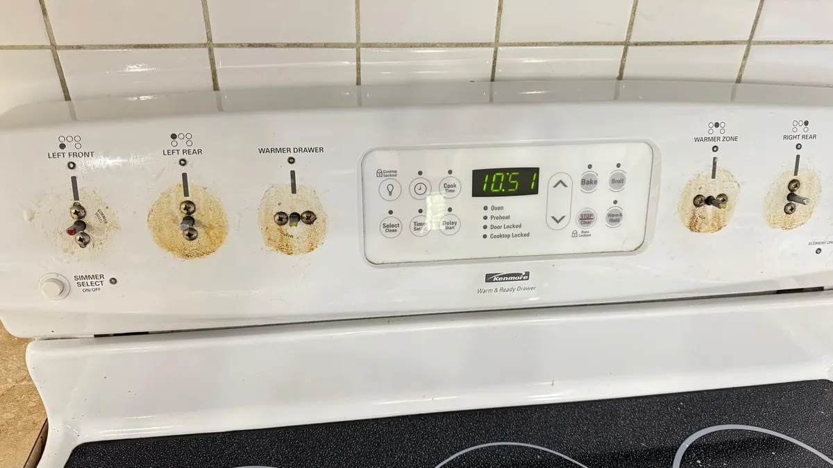 Stove control panel with grease buildup around the knobs before professional cleaning